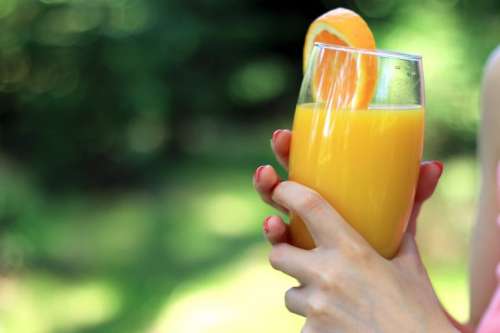 Glass of orange juice in the hands of woman in nature
