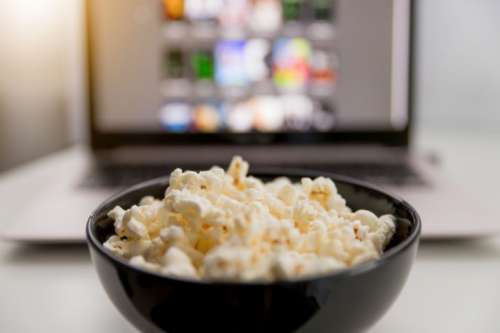 Watching movies online on laptop and eat popcorn.