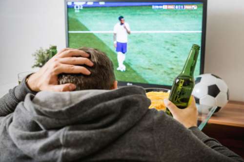 Young man watching football sport on tv at home.