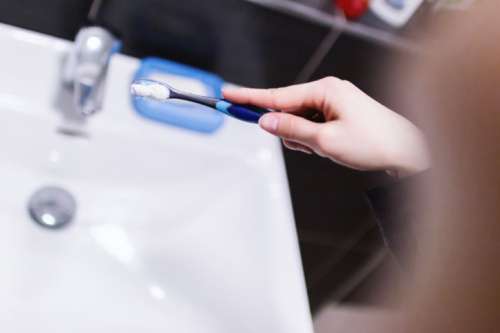 Woman hand holding toothbrush with toothpaste applied on it in bathroom