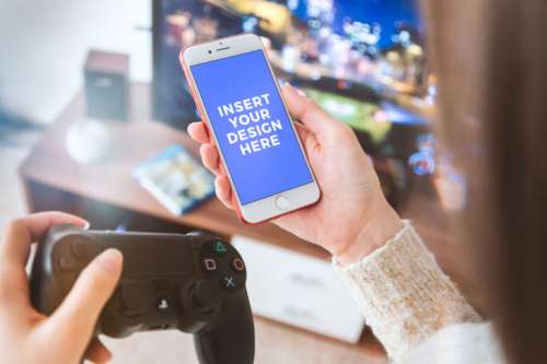 Player with PS4 gamepad use his smartphone at home. Free PSD Mockup
