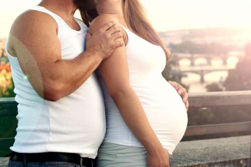 Pregnant woman with her husband standing together near city views