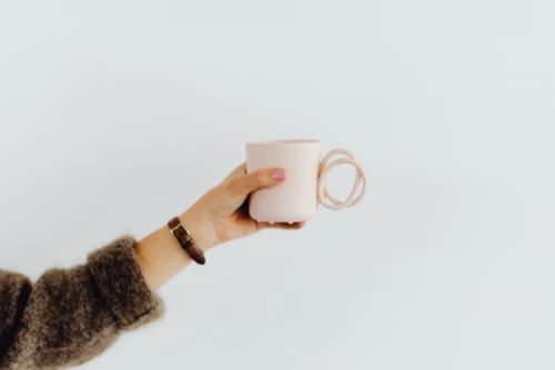 A woman in a brown sweater holds a pink, minimalist mug