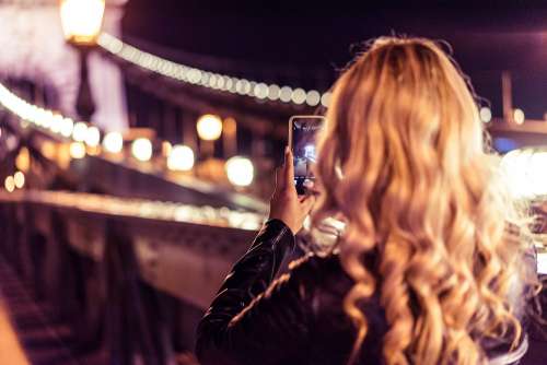 Blonde Woman Taking a Photo of an Old Bridge at Night