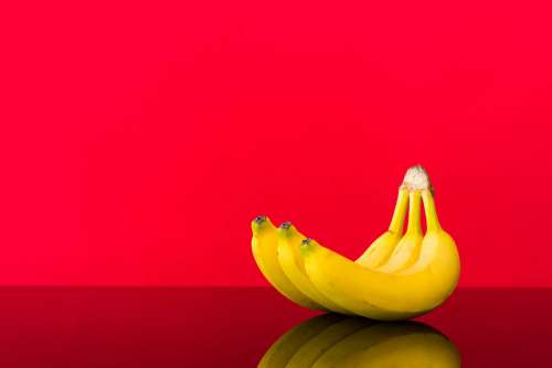 Fresh Bananas on Glossy Table and Red Background