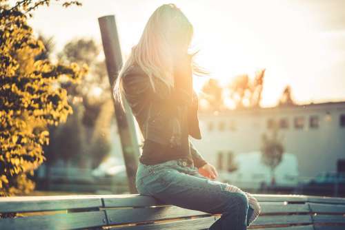 Blonde Woman Sitting Alone on a Bench Against Sunset