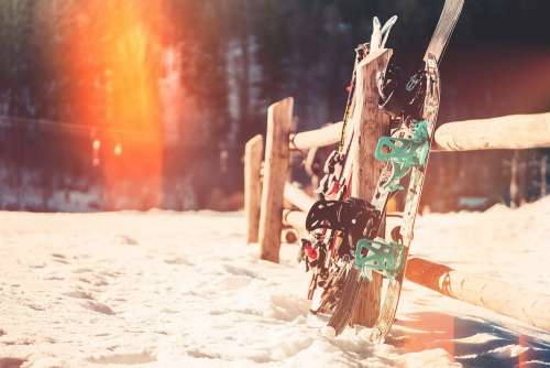 Snowboards and Skis Leaning Against Wooden Fence