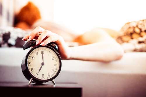 Woman Shutting Off Ringing Alarm Clock From Bed
