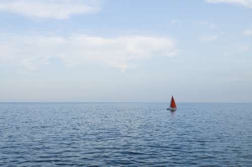 Sail boat with a red sail cruising in the calm waters of the evening.