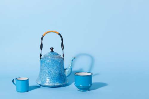 A Blue Kettle And Tin Mug Against A Blue Background Photo