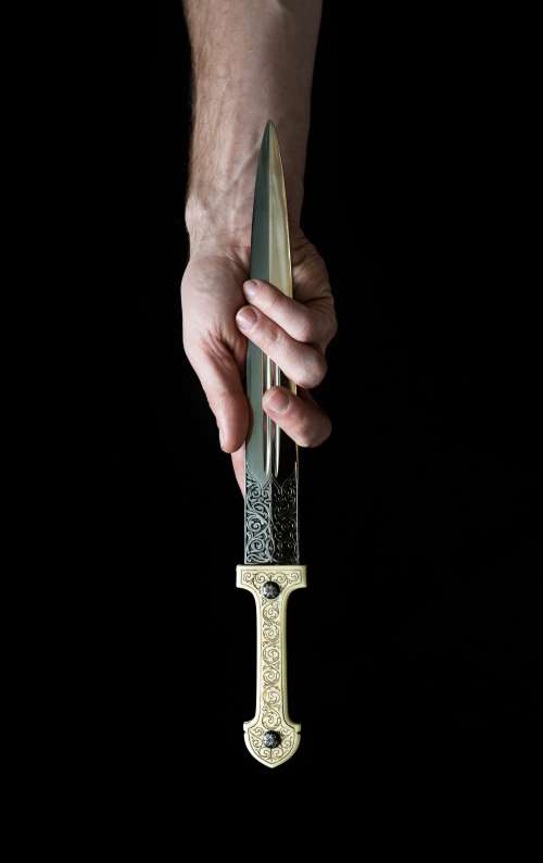 A Hand Clasps An Ornate Dagger By The Blade Photo