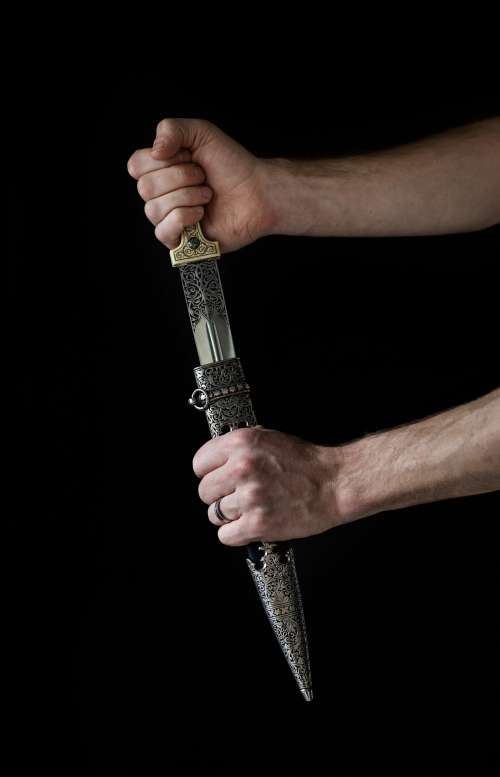 A Hand Draws An Ornate Dagger From Its Sheath Photo