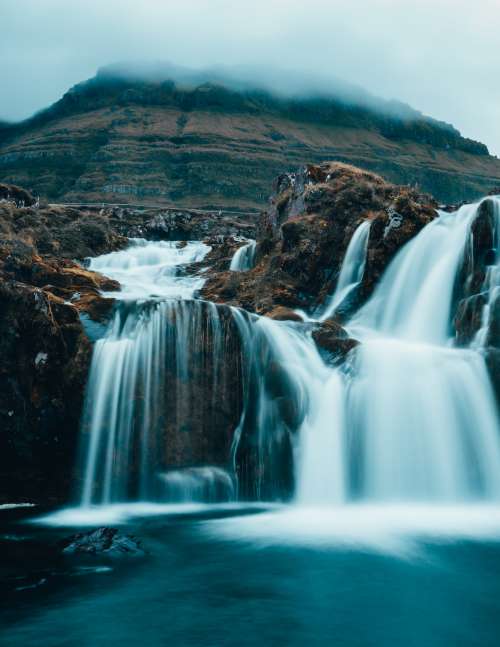 Cloudy Waterfall At The Base Of A Mountain Photo