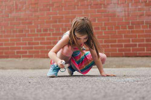 Girl Using Sidewalk Chalk In Schoolyard Photo