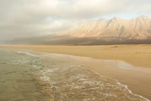 Tall Mountains Look Over Ocean And Sandy Beach Photo