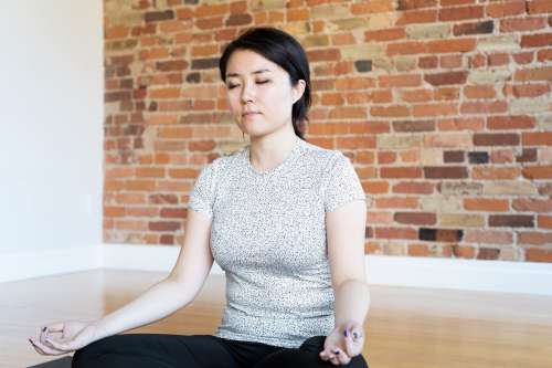 Young Woman Meditating In Front Of Brick Wall Photo