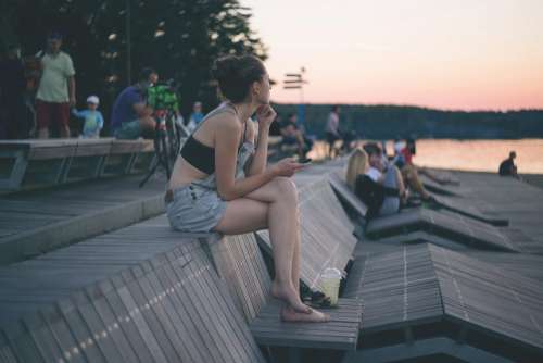 A girl with the phone sitting at the lake