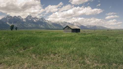 Beautiful Landscape with grassland and Mountains with Cabin under sky and clouds free photo