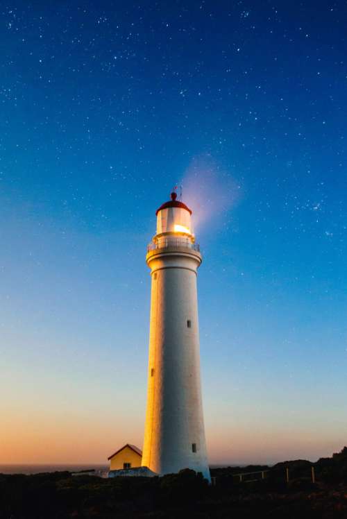 Lighthouse beneath the sky and stars with light on free photo