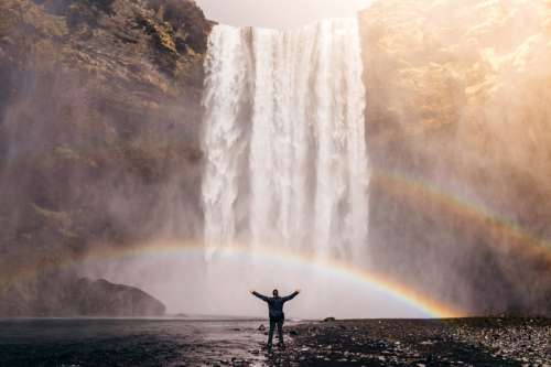 Man Standing Beneath the Waterfall and Double Rainbow free photo