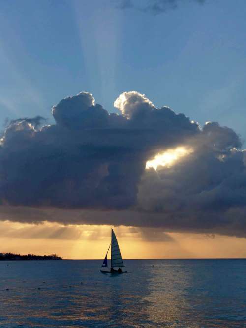 Sailboat under a clump of clouds at sunset in Jamaica free photo
