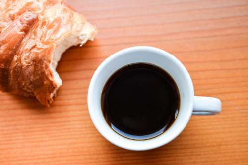 Black coffee in white cup with a croissant