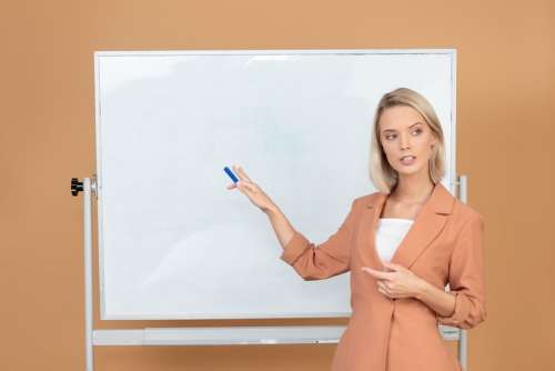 Young Attractive Teacher Explaining Something Standing Next To A Whiteboard