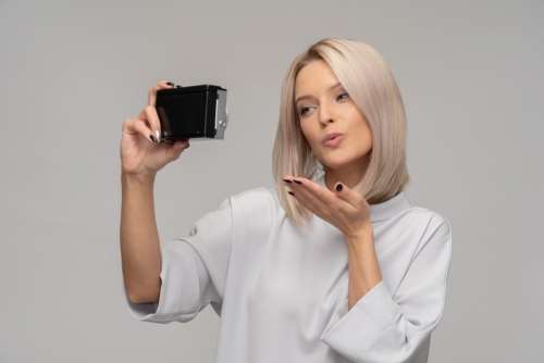 Young Woman Taking A Selfie With An Old Camera And Sending Air Kiss