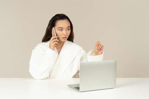 Young Asian Woman Talking On The Phone And Using Laptop