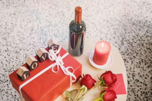 Wooden table with bottle of wine, roses and gift box