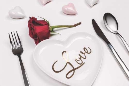 Fork, knife and spoon with red rose on white table. Love concept