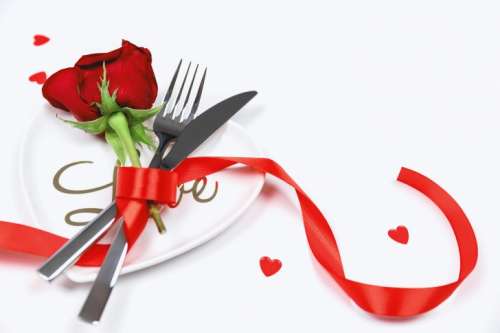 Fork, knife and spoon with red rose on white table. Love concept