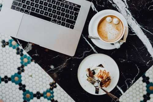 Laptop, coffee and cake with meringue and whipped cream on black marble