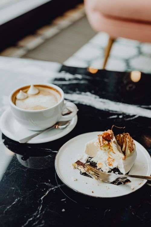 Laptop, coffee and cake with meringue and whipped cream on black marble