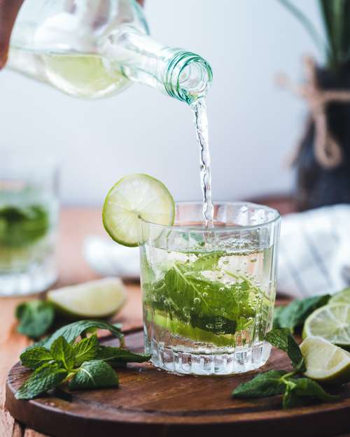 Pouring water in a glass with mint and lime