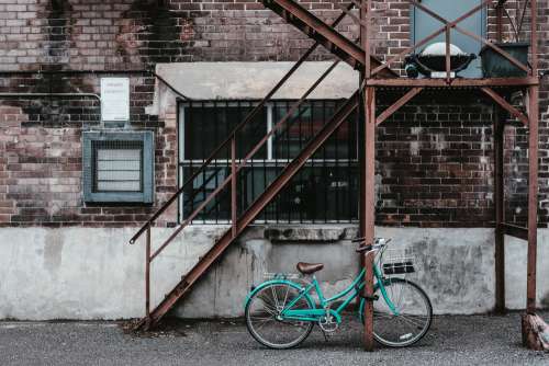 A Blue Bicycle Against A Rusty Apartment Fire Escape Photo