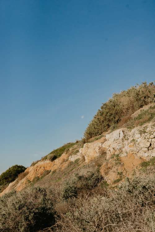 White Moon On Crisp Blue Daytime Sky Lined By Rocky Cliffs Photo