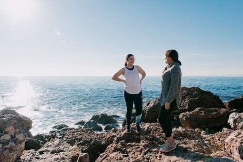 Women In Activewear Take A Moment To Share A Laugh On Beach Photo