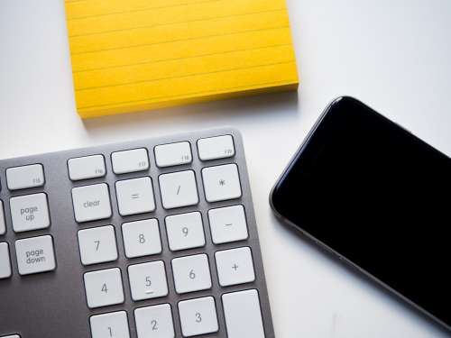 Keyboard, Phone, and Yellow Note on White Desk