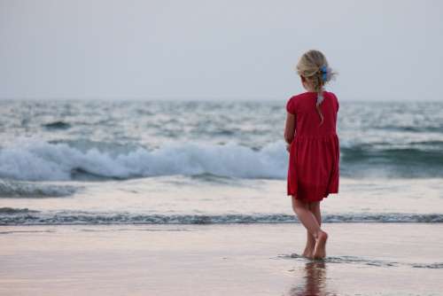 Beautiful Blonde Little Girl Dressed in a Red Dress Playing on the Beach