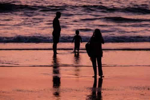 Silhouettes of Parents Taking Photos of Their Son on the Beach at Sunset