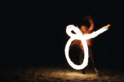 A Fire Dancer Draws Shapes On A Beach At Night Photo