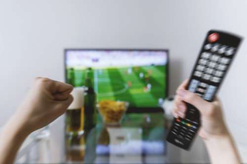 Watching football match on tv with remote controller.