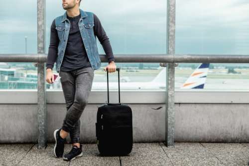 Male tourist is standing outdoor in airport with a luggage