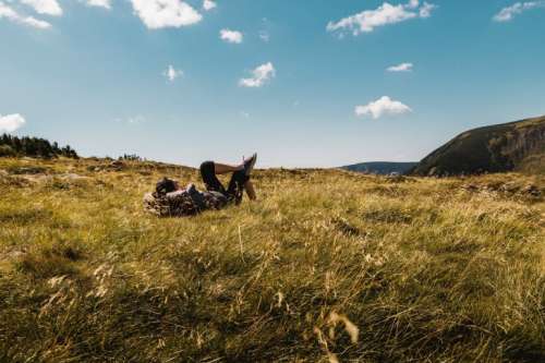 Carefree happy woman lying on green grass meadow on top of mountain