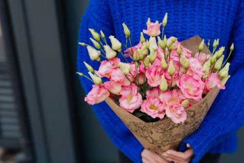 Close up of woman holding bouquet of pink lisianthus flowers wrapped in brown paper