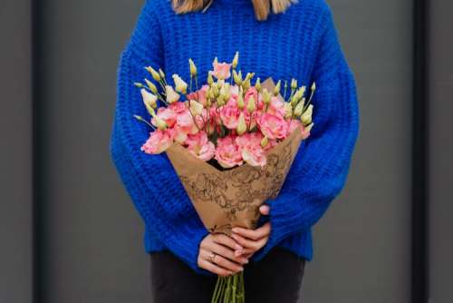 Close up of woman holding bouquet of pink lisianthus flowers wrapped in brown paper