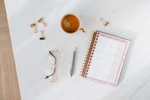 Top view of a marble desk with coffee, notebooks and pen