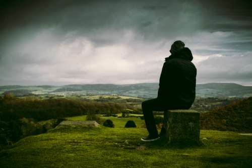 man enjoying landscape sitting rock
