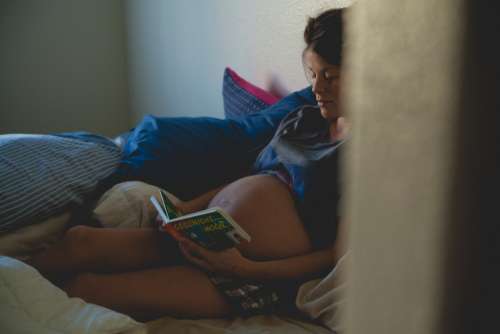 pregnant woman reading book bed